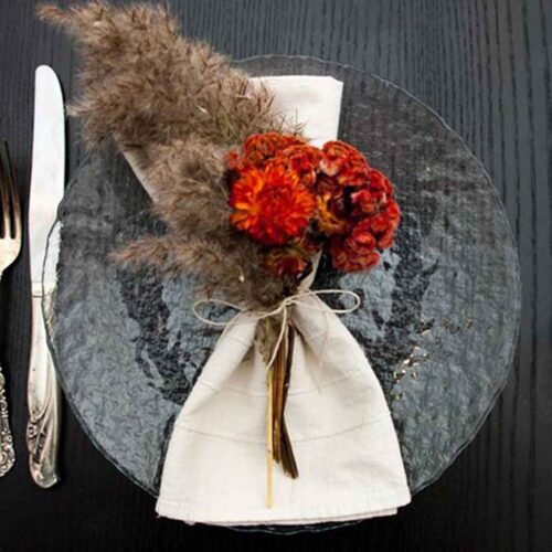 A clear plate on a black table with a napkin and bright dry flowers tied to it with string.