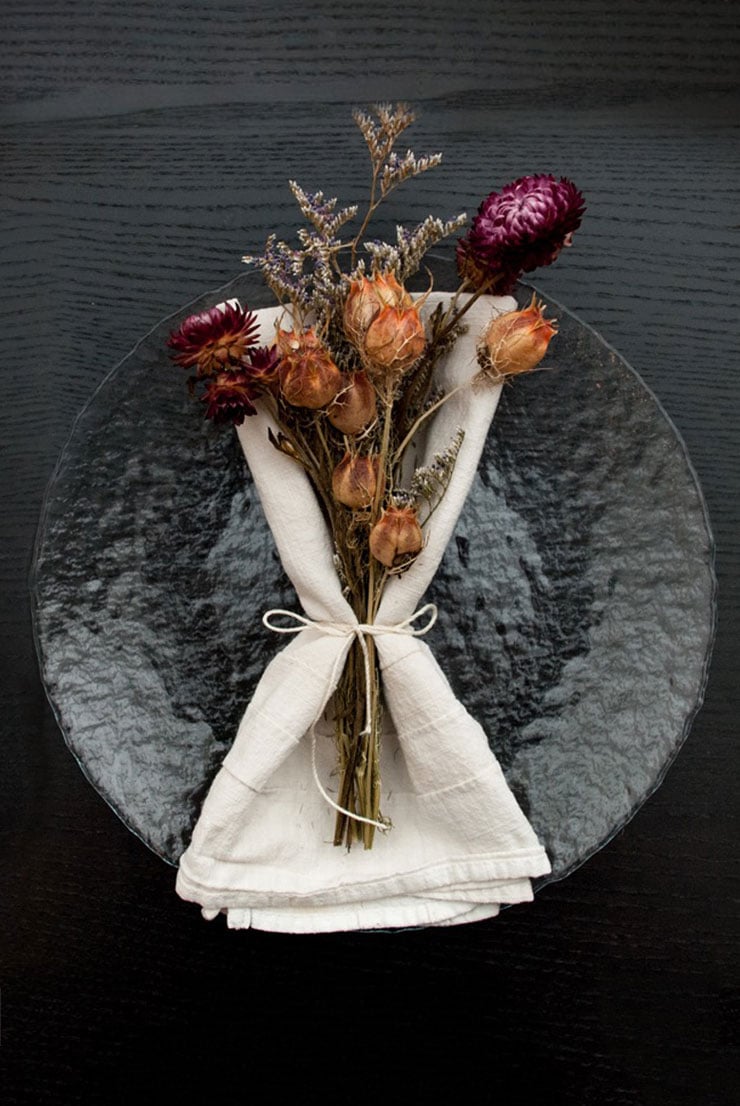 A clear plate on a black table with a napkin and bright dry flowers tied to it with string.