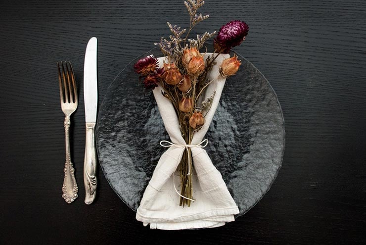 A clear plate on a black table with a napkin and bright dry flowers tied to it with string.