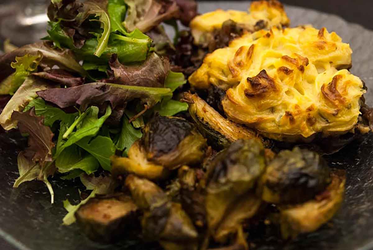 A plate with shepherd's pie, brussels sprouts and a simple salad.