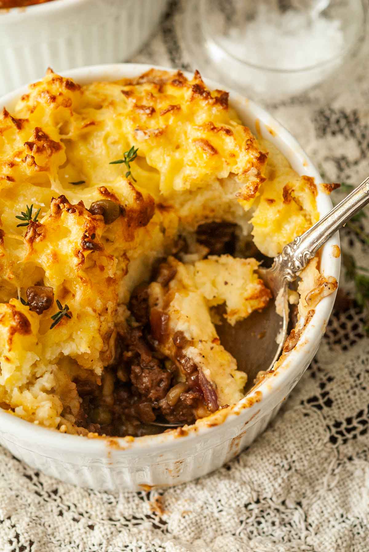 A half-eaten shepherd's pie with a spoon on a lace table cloth.