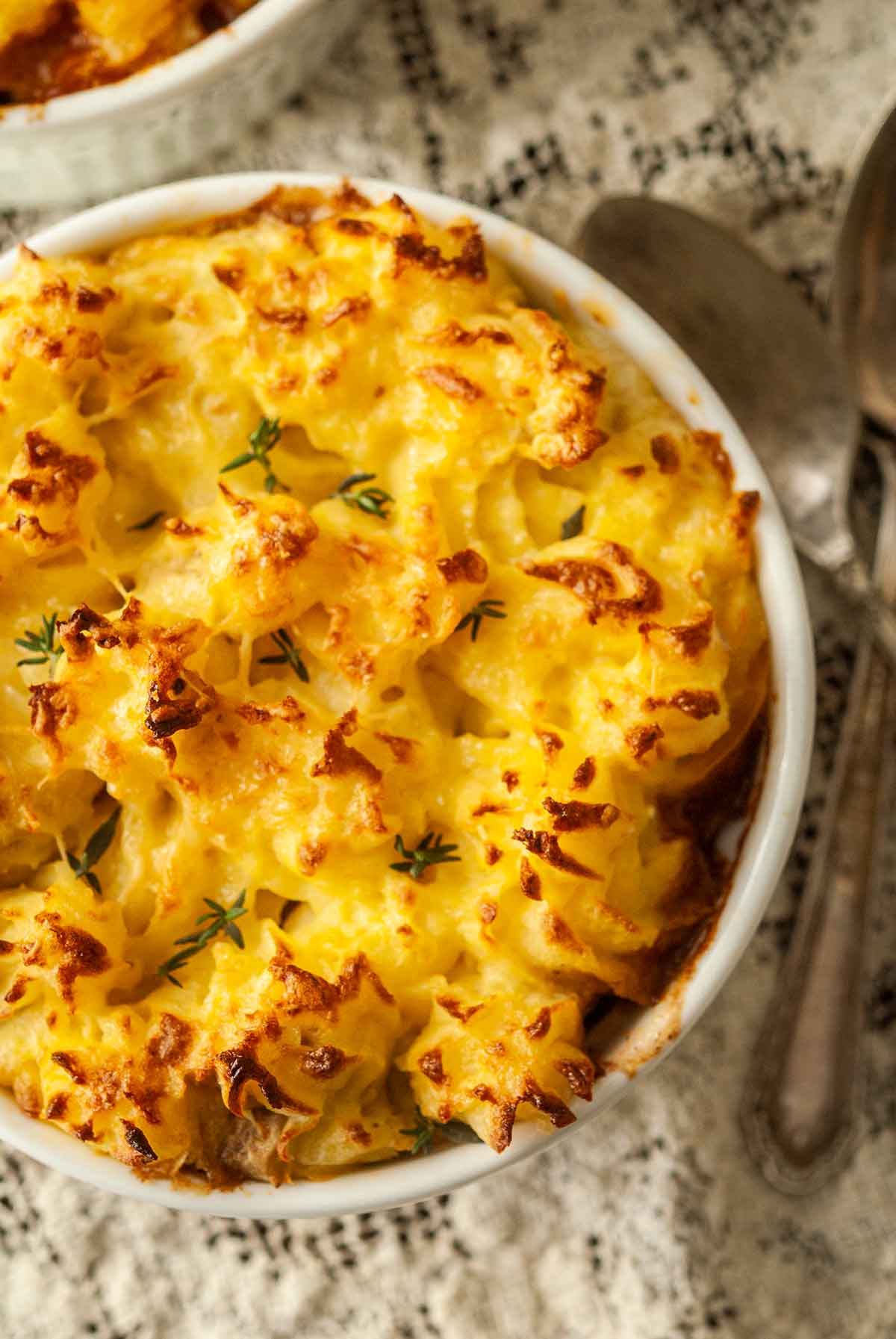 Baked shepherd's pie in a bowl on a lace table cloth beside a spoon.