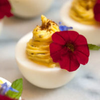 A deviled egg on a marble plate garnished with a flower beside 3 others out of frame.