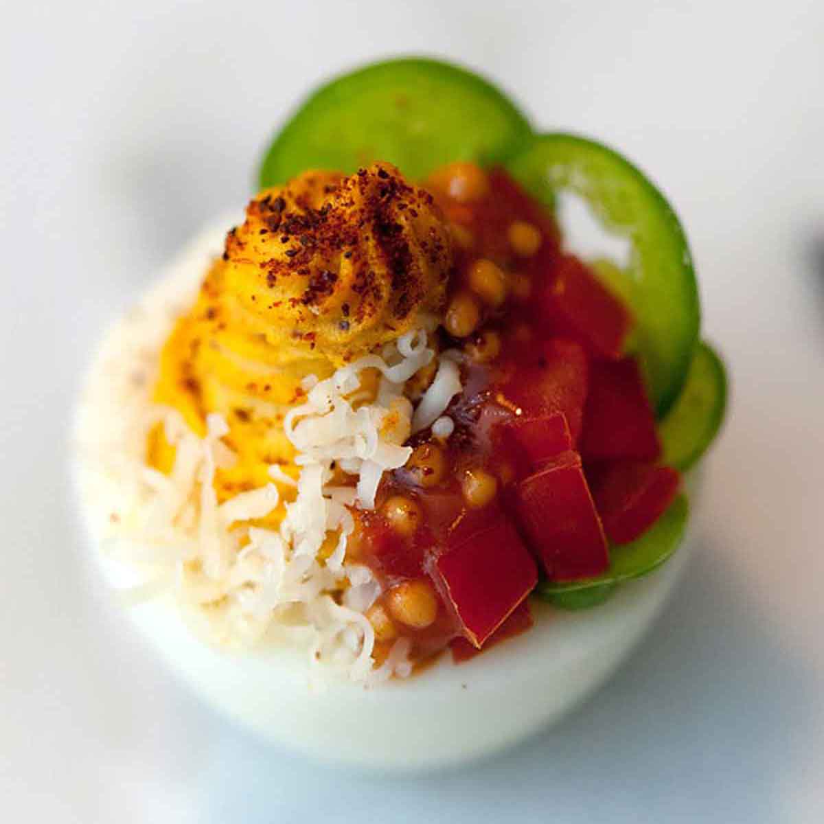 A deviled egg, garnished with sliced jalapeños, diced tomatoes, mustard caviar, shredded cheese and paprika.