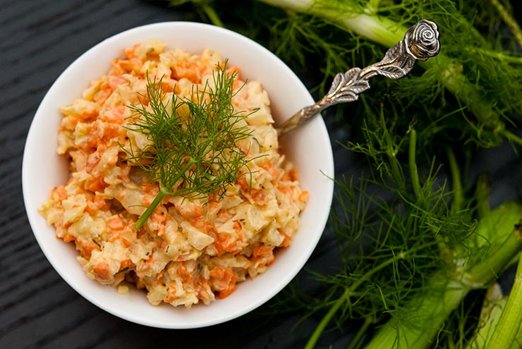 A small bowl of fennel coleslaw, topped with dill, on a table.