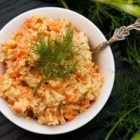 A small bowl of fennel coleslaw, topped with dill, on a table.