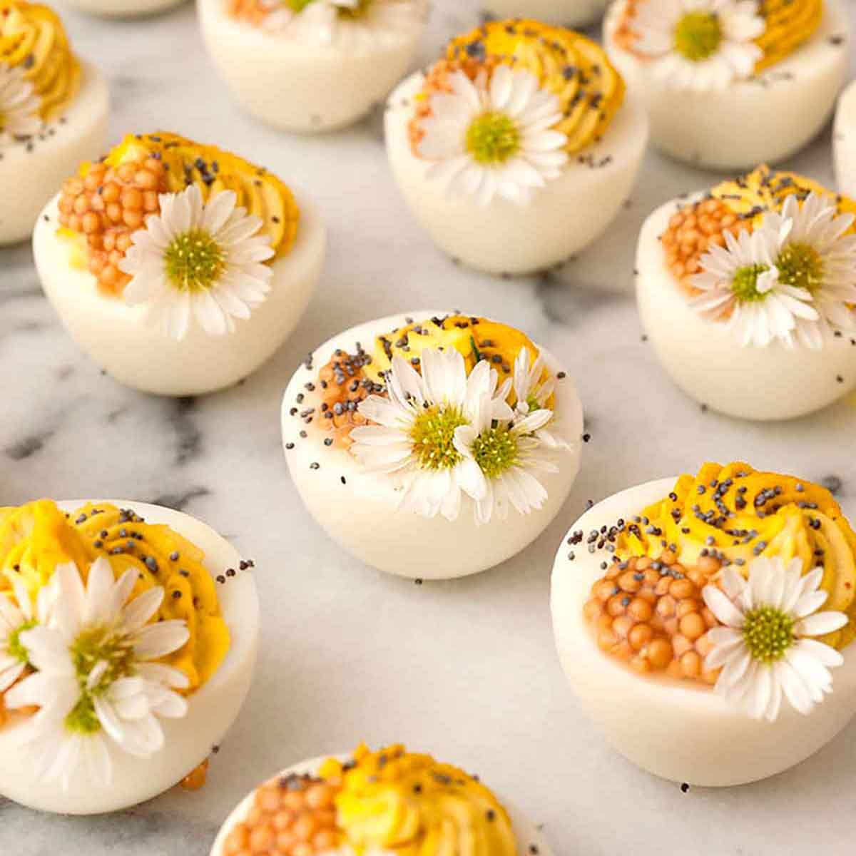12 deviled eggs on a marble plate garnished with daisies and mustard caviar.