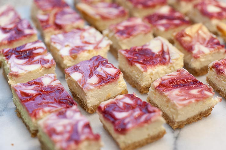 Raspberry marbled lemon cheesecake bars on a marble table.