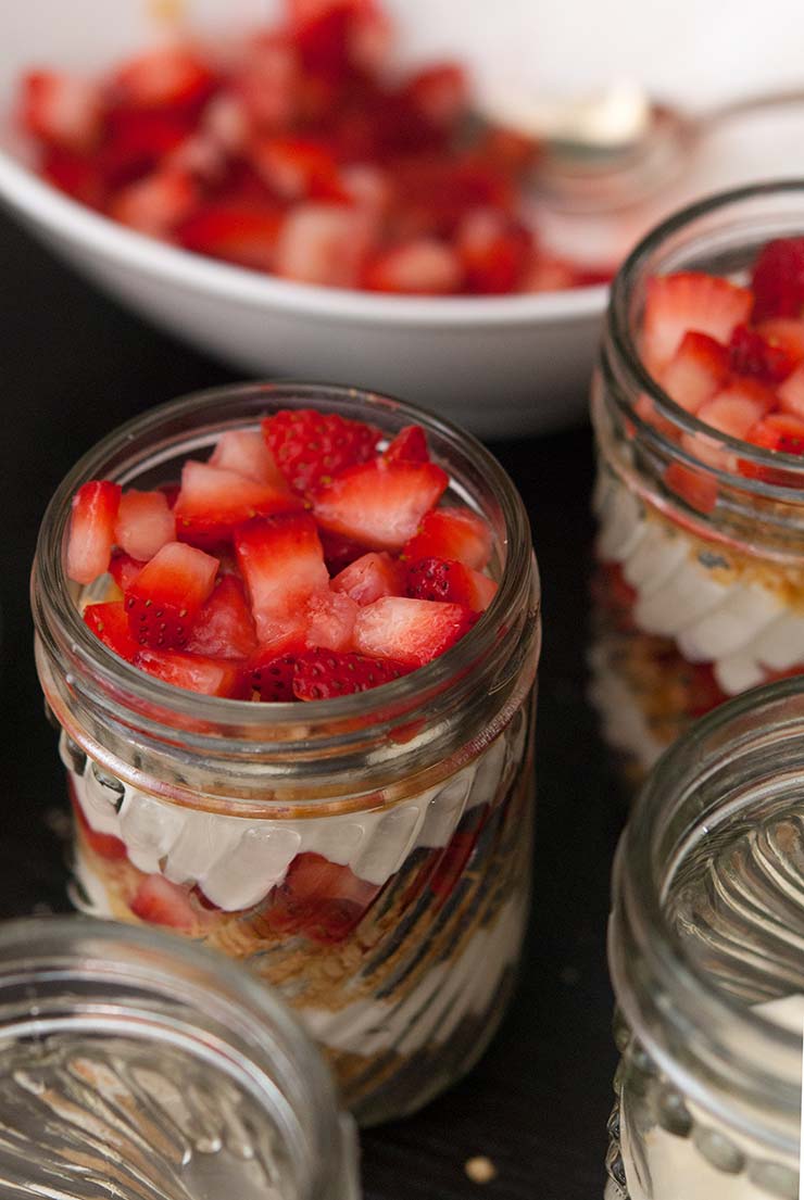 A jar of lemon mousse parfait topped with chopped strawberries on a table beside other filled jars.