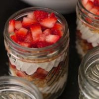 A jar of lemon mousse parfait topped with chopped strawberries on a table beside other filled jars.