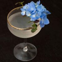 A cocktail garnished with flowers and greenery on a dark table.