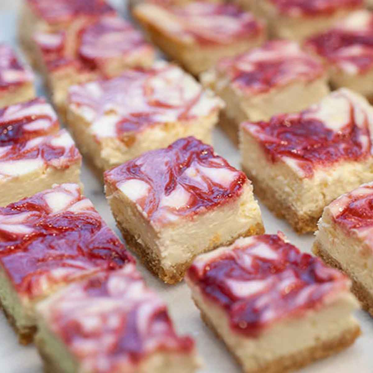Raspberry marbled lemon cheesecake bars on a marble table.