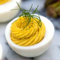 A deviled egg on a marble plate, garnished with a sprig of dill.