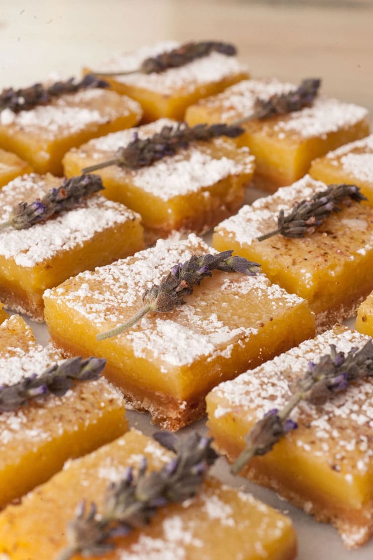 Lavender lemon bars on a white marble table garnished with fresh lavender and powdered sugar.