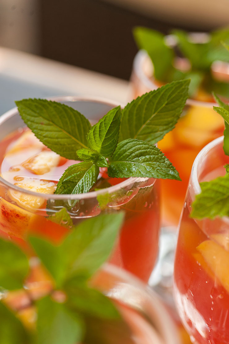 This tropical watermelon sangria is like a Hawaiian vacation in a glass! Fresh squeezed watermelon juice, coconut and sparkling citrus flavors make this a perfect pool party signature cocktail. #cocktails, #sangria The mint garnish on a glass of sangria, beside 3 other glasses.