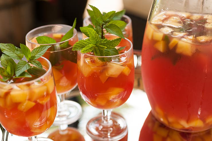 This tropical watermelon sangria is like a Hawaiian vacation in a glass! Fresh squeezed watermelon juice, coconut and sparkling citrus flavors make this a perfect pool party signature cocktail. A silver tray with 4 glasses of fruit-filled watermelon sangria, garnished with mint, next to a full pitcher.