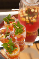 A silver tray with 4 glasses of fruit-filled watermelon sangria, garnished with mint, next to a full pitcher.