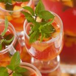 A sangria cocktail garnished with mint, filled with fruit, on a serving tray beside 3 other glasses of sangria.