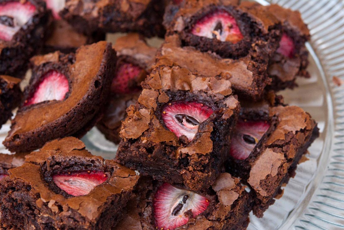 Brownies garnished with strawberries on a glass plate.