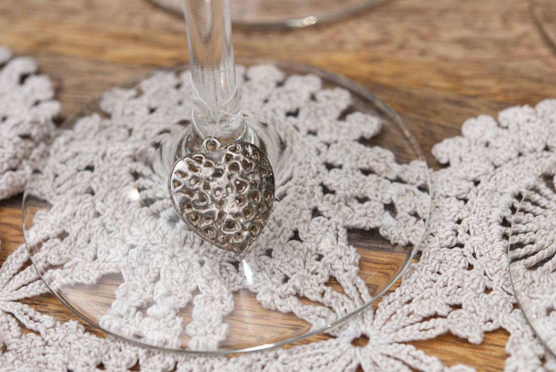 A heart shaped charm tied with thread to the base of a wine glass on top of a doily.