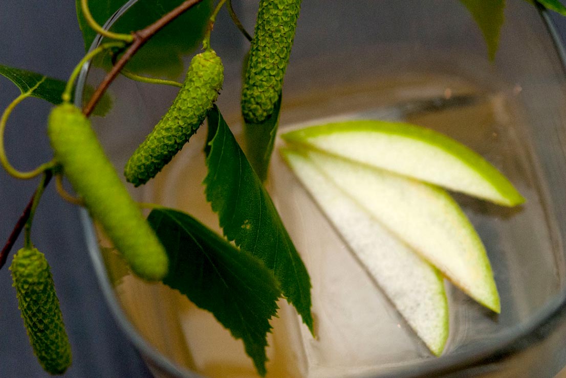 A large ice cube and 3 slices of green apple fanned out on top in a cocktail.