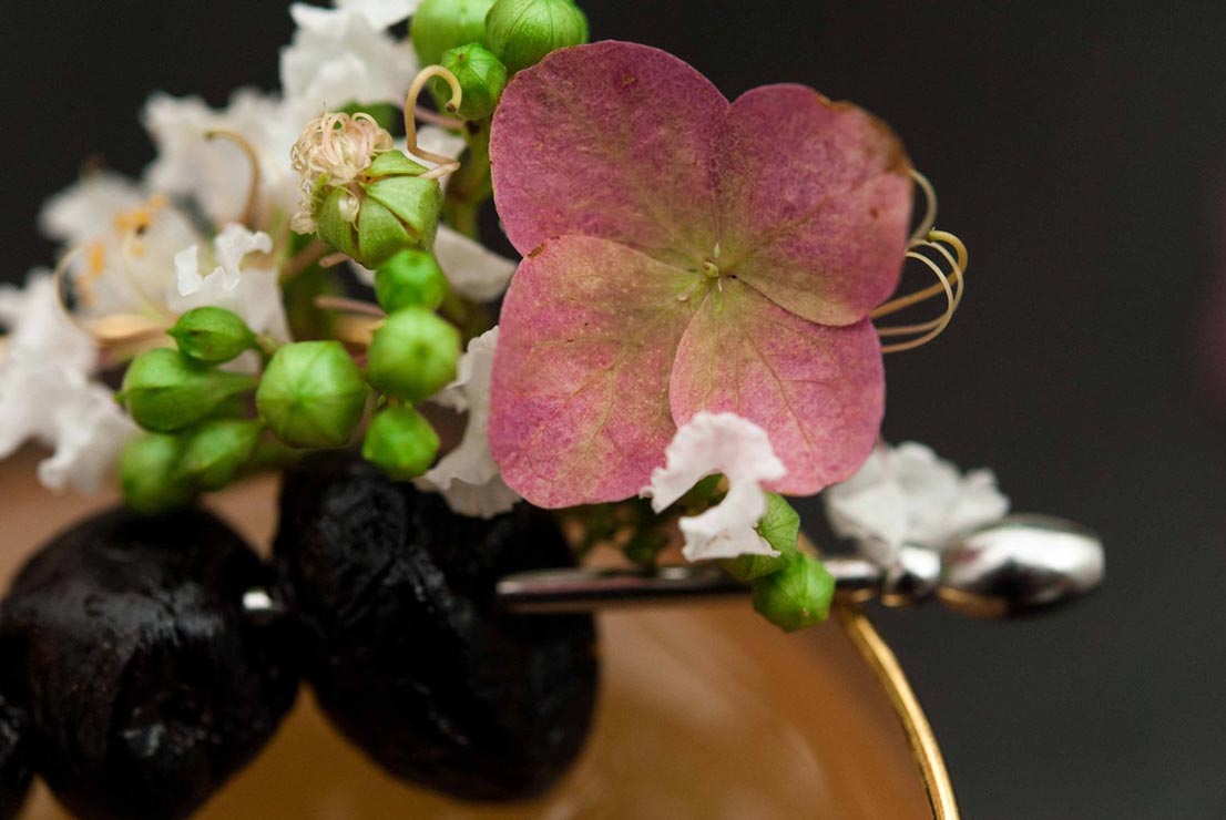 A cocktail garnish of flowers and olives.