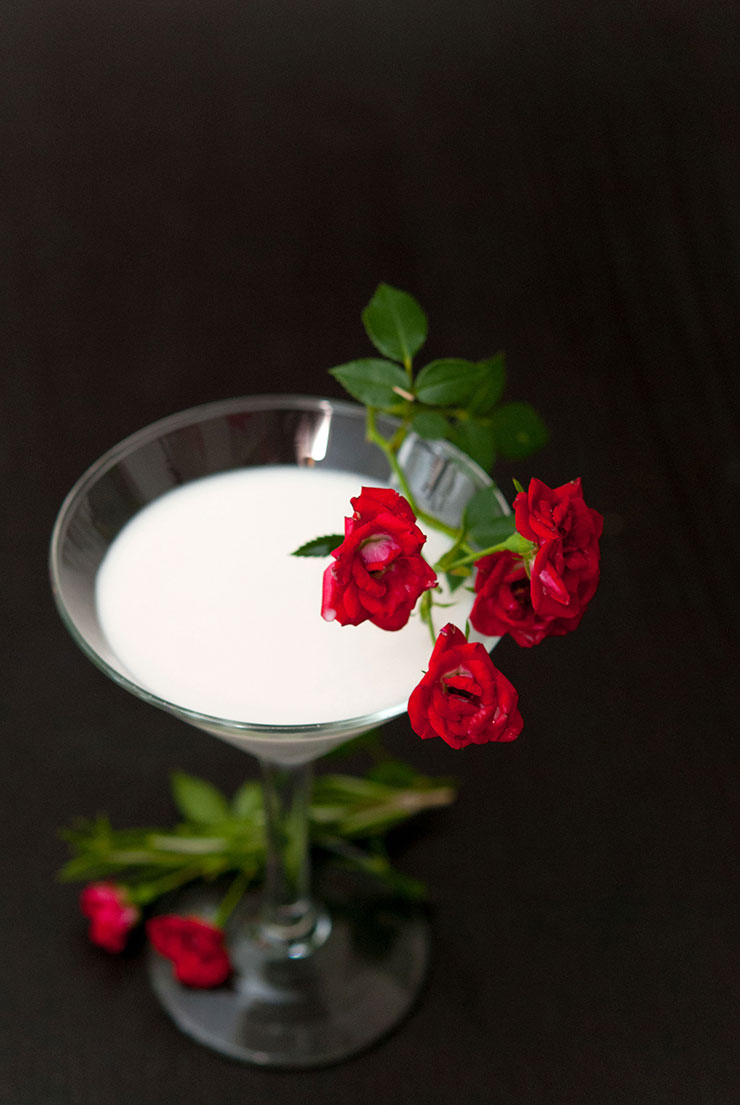 A white cocktail in a martini glass garnished with red roses.