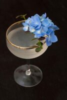 A cocktail garnished with flowers and greenery on a dark table.
