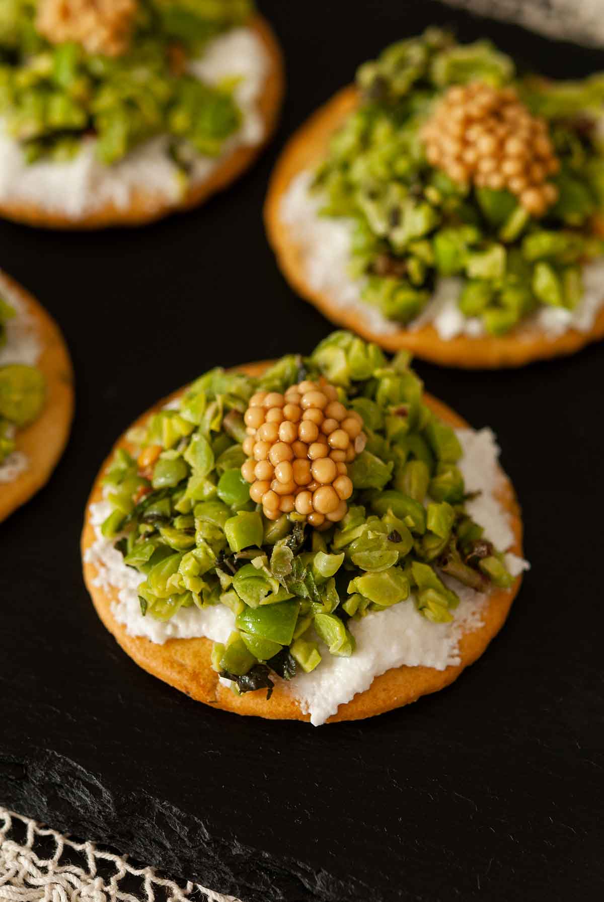 3 spring pea appetizers topped with mustard caviar on a slate.