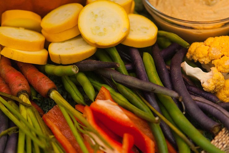 A closeup of sliced yellow squash, green and purple beans, peppers and carrots.