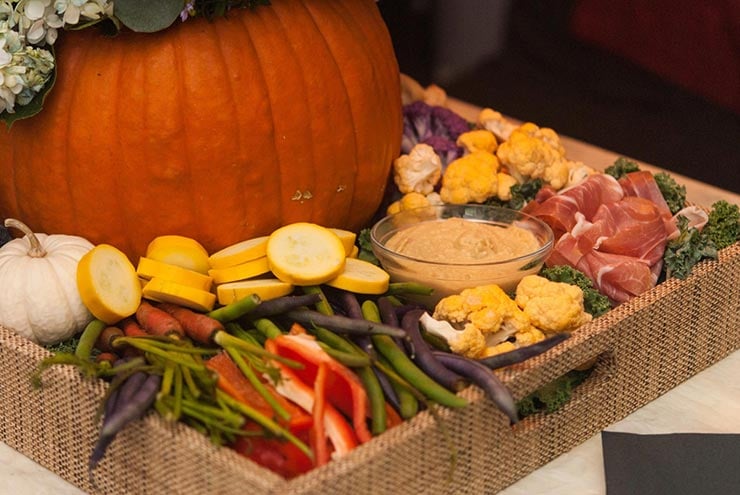 A tray with assorted vegetables, a bowl of hummus and prosciutto next to a pumpkin in the center the tray.