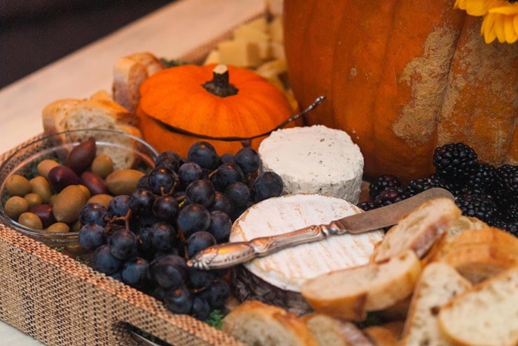 A tray full of cheese, grapes, bread, and olives with a small pumpkin gourd cut like a bowl.