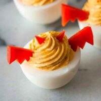 3 deviled eggs garnished with horns and wings made of red pepper on a marble board.