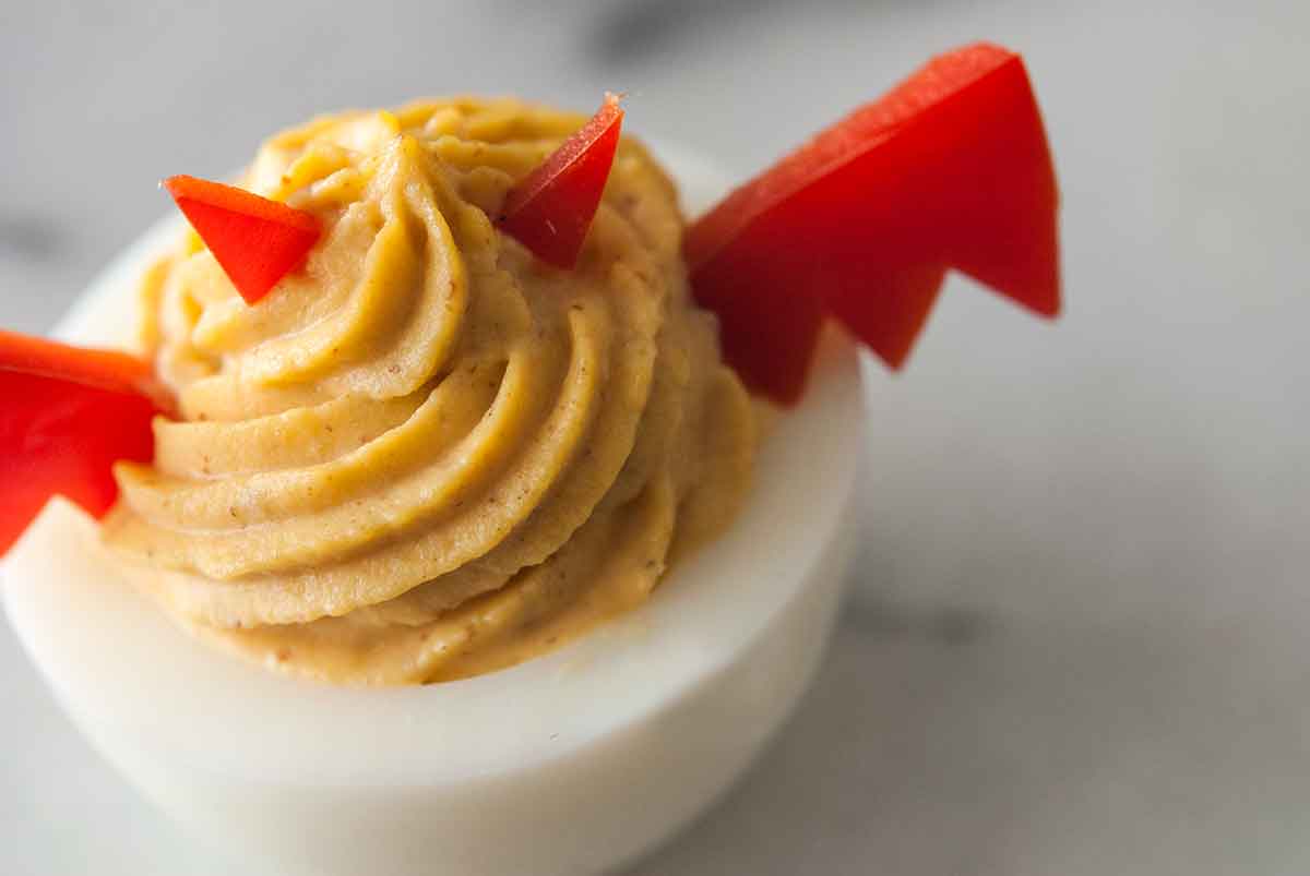 A deviled egg garnished with horns and wings made of red pepper on a marble board.