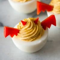 A deviled egg with bell pepper horns and wings on a marble plate with 2 others in the background.