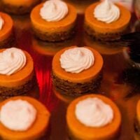 12 mini-pumpkin pies on a silver tray with whipped cream on top.