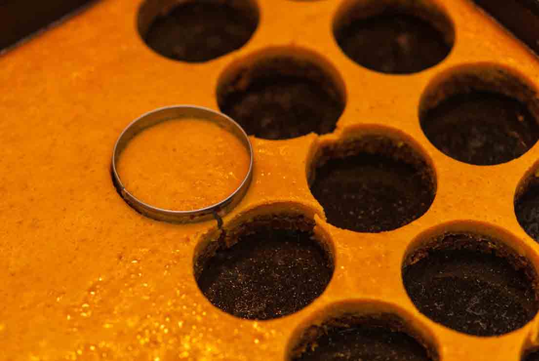 A cookie cutter cutting mini pumpkin pies out of a baking tray.