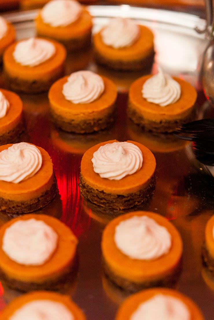 12 mini-pumpkin pies on a silver tray with whipped cream on top.