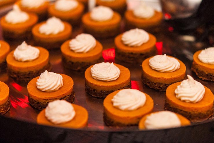 12 mini-pumpkin pies on a silver tray with whipped cream on top.