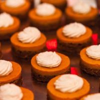 12 small pumpkin pies, topped with whipped cream on a metal tray.