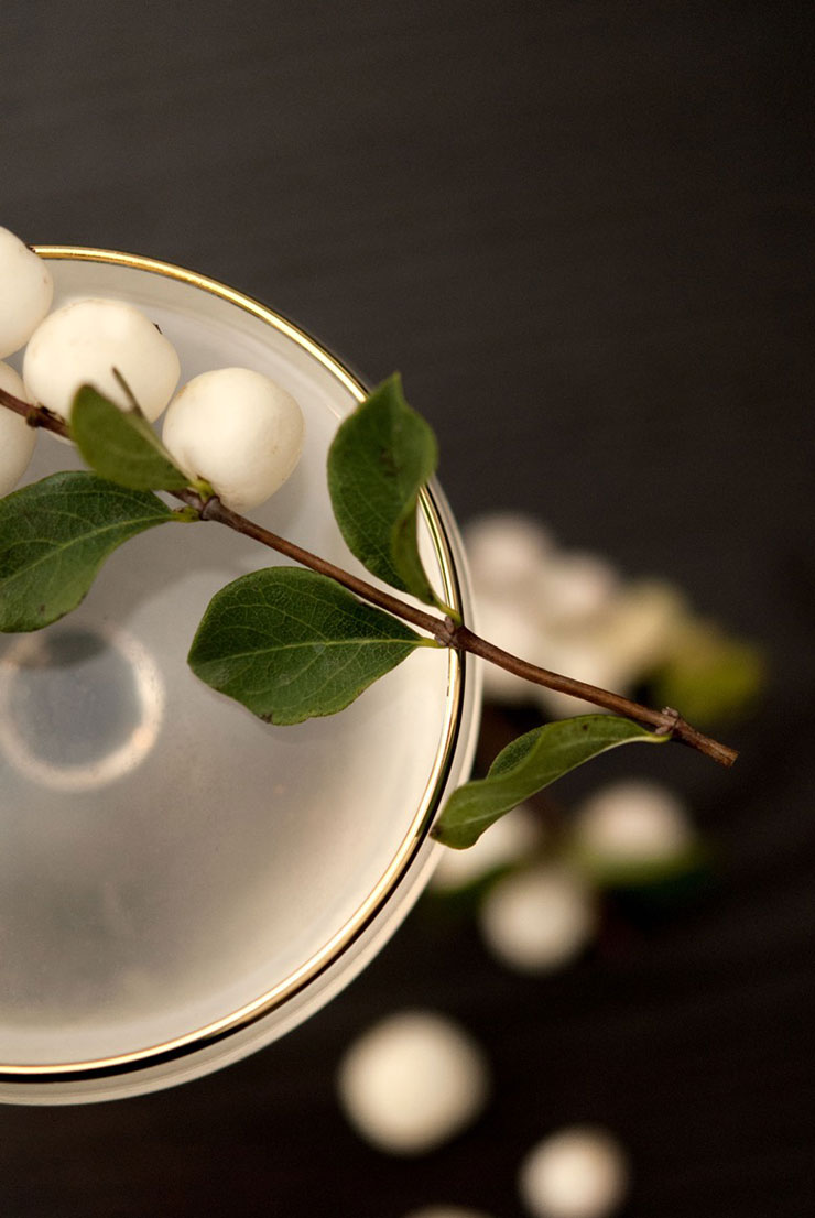 Ghost berries on top of a sake cocktail from above, with a few ghost berries sprinkled on the black table below.