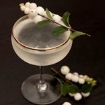 A cocktail, garnished with white berries on the edge, with a few berries at its base.