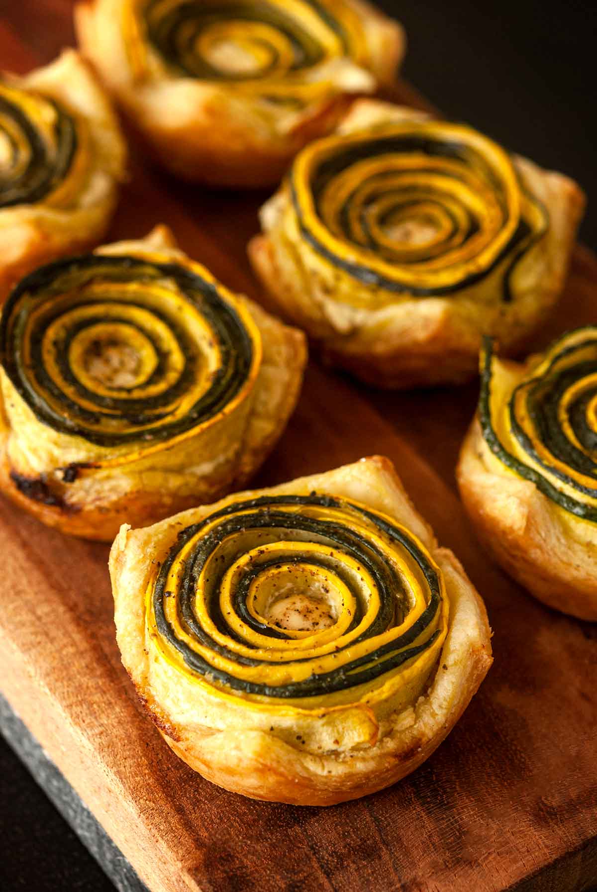 6 pesto zucchini rosettes on a wooden board.