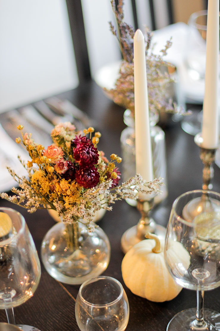 A place-setting with white candles in silver candle sticks, white pumpkins and stemware on a black table.