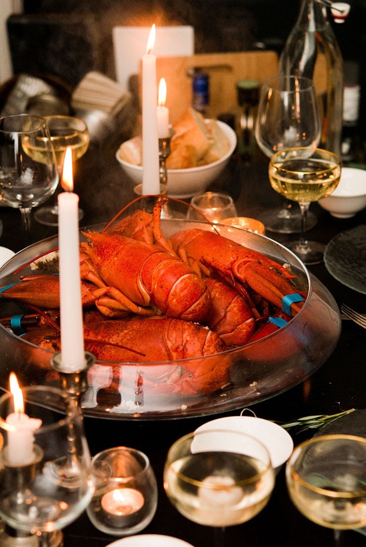 A table with a large bowl of cooked lobsters in the center, surrounded by glasses, candles and cutlery.
