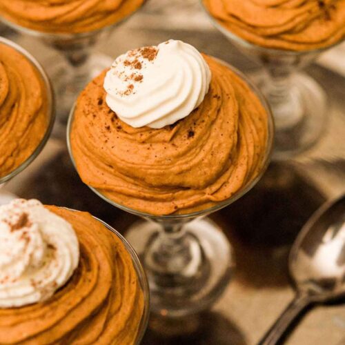 5 small glasses full of pumpkin mousse topped with whipped cream, sitting on a silver tray.