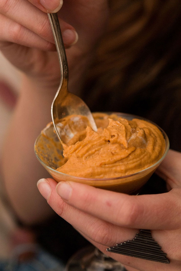 A hand sinking a silver spoon into a glass of pumpkin mousse.