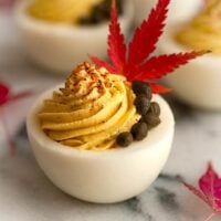 A deviled egg garnished with capers, a single leaf, and sprinkle of spices on a marble plate.