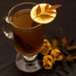 A mug of hot toddy, garnished with an orange slice, topped with a small lead, with a few dry roses and leaves at its base.