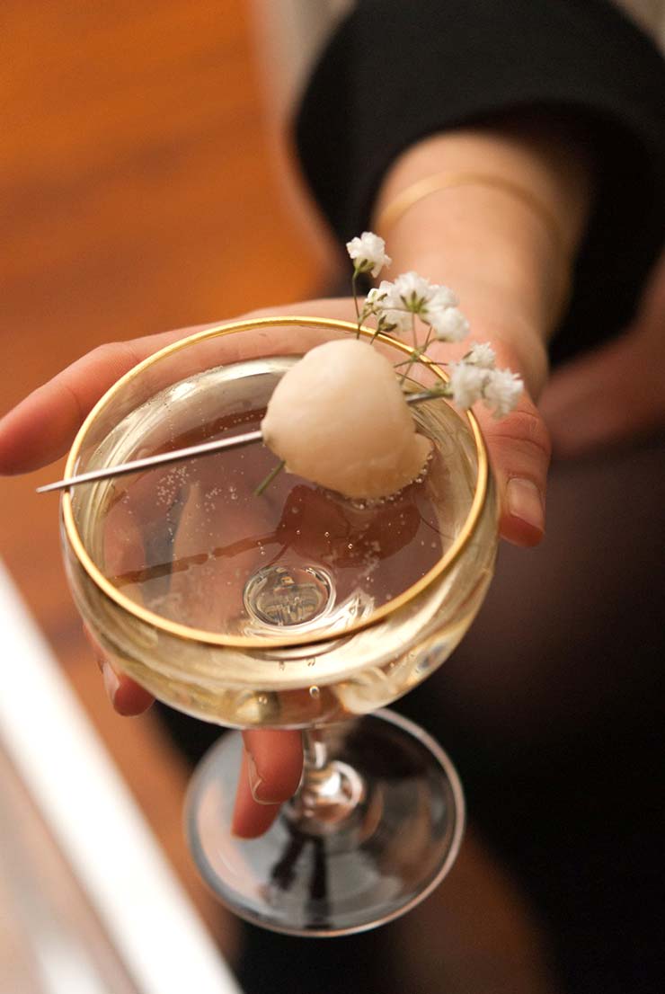 A hand holding a cocktail garnished with a lychee and baby's breath.